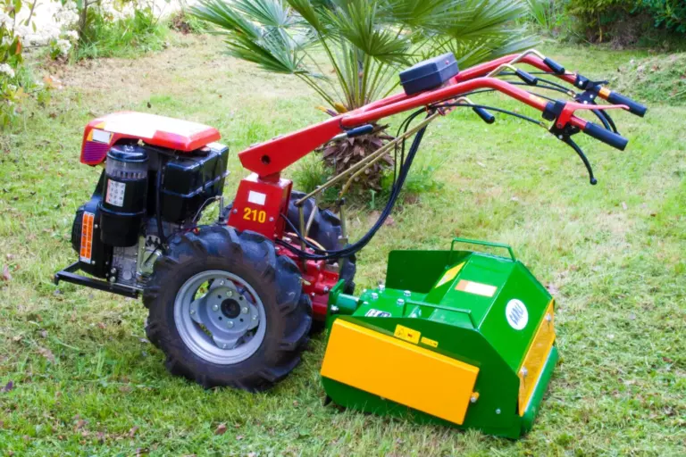 La trincia montata su un motocoltivatore rosso, ferma sul prato di un giardino.