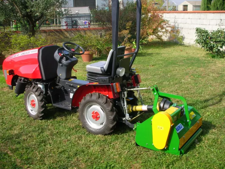 La trincia montata dietro un mini trattore rosso, fermo sul prato di un giardino.
