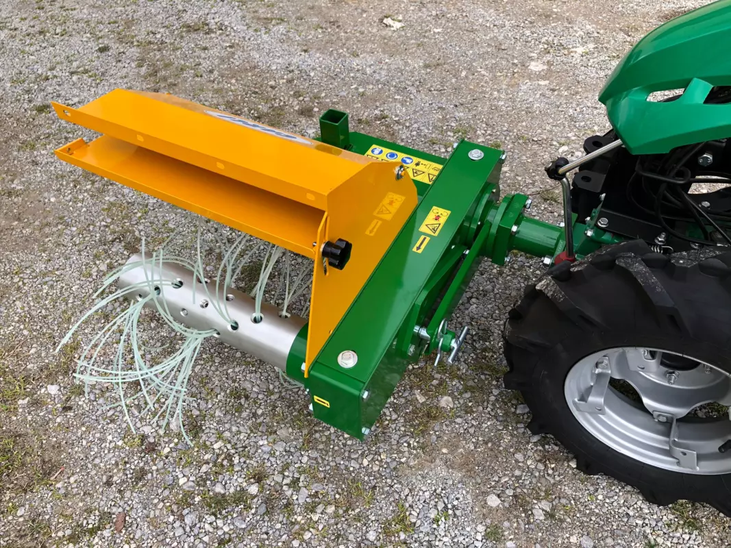 Decespugliatrice DT300 con telaio verde e carter giallo montata su un motocoltivatore verde, su ghiaia: si vedono l’albero con i fili da decespugliatore e la flangia di attacco.
