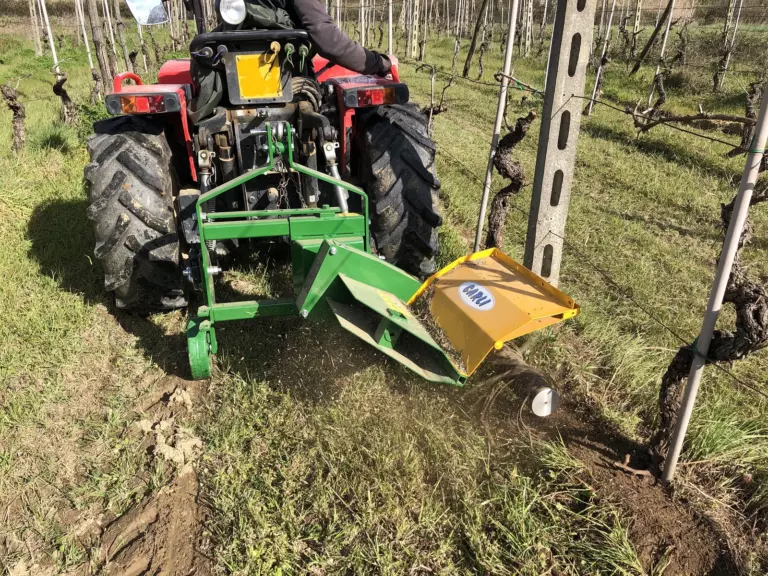 La decespugliatrice montata dietro un trattore rosso, al lavoro in un vigneto: l’albero con i fili pulisce l’erba sotto il filare.