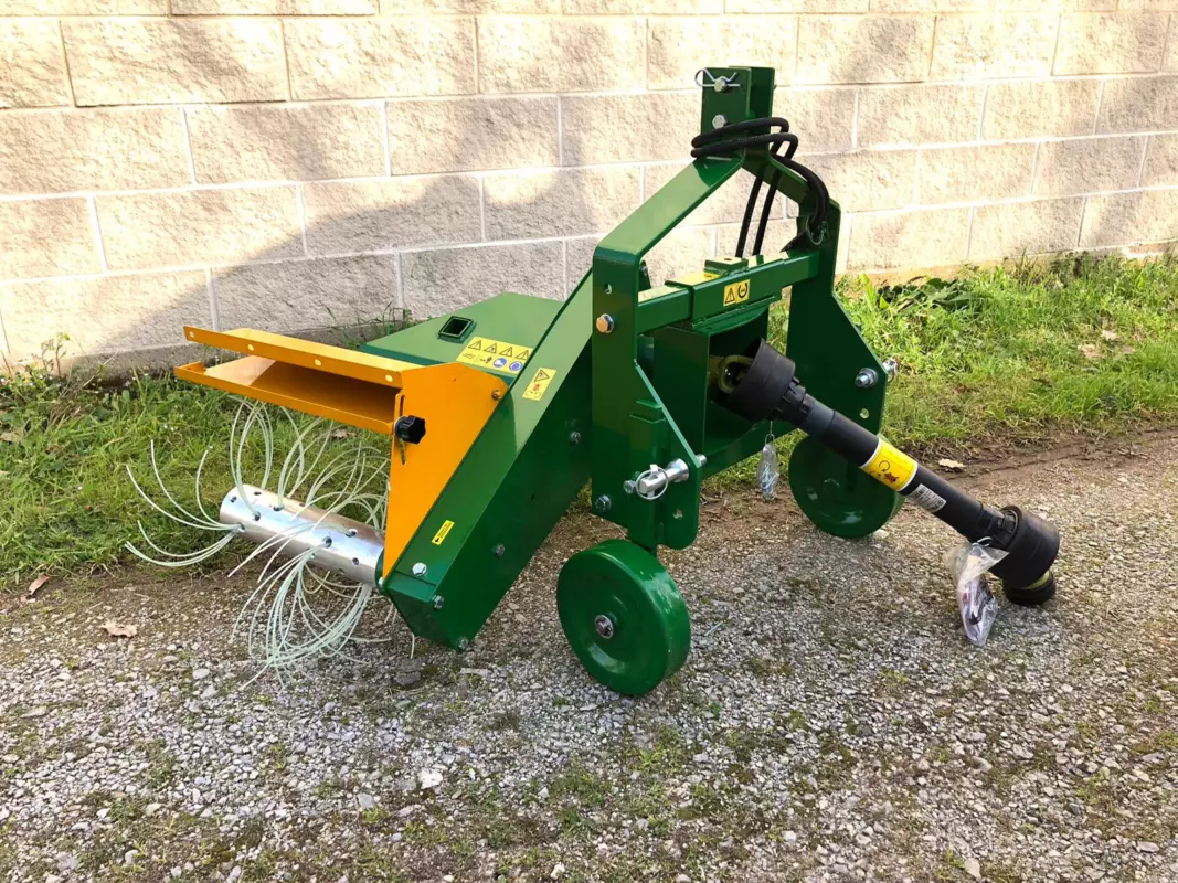Decespugliatrice DT5003P verde e gialla appoggiata su ghiaia davanti a un muro, con il castello di attacco a 3 punti, l’albero con i fili da decespugliatore e l’albero cardanico collegato.
