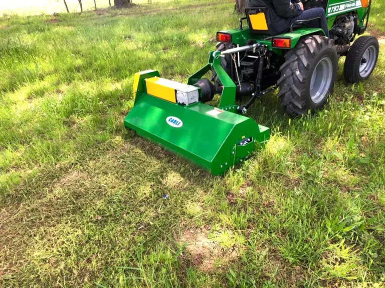 La trincia montata dietro un piccolo trattore verde, su un prato.