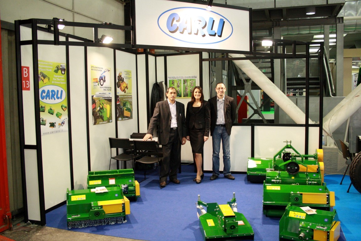 Tre persone dello staff Carli allo stand dell’azienda in una fiera, tra le trince verdi e gialle